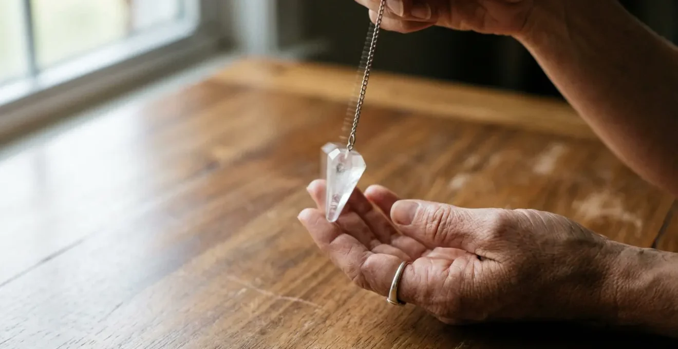 Mani che tengono un pendolo di cristallo sopra una superficie di legno naturale con luce dorata